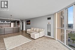 Open concept living area featuring floor-to-ceiling windows, tile flooring, a breakfast bar, recessed lighting, and a modern chandelier - 
