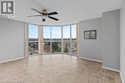 Expansive living space featuring large bay windows, neutral tile flooring, a ceiling fan, and light gray painted walls - 