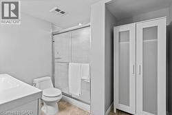 Bathroom featuring a glass-enclosed shower with tiled walls, a white vanity with an integrated sink, a commode, and a white storage cabinet with frosted glass panel doors - 