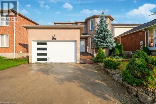 Brick exterior featuring a modern garage door with rectangular windows, paved driveway, and established landscaping - 888 Paisley Road, Guelph, ON - Outdoor