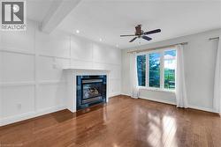 Living area featuring a fireplace with a dark tile surround and white mantle, white paneled accent wall, wood-finish flooring, recessed lighting, and a ceiling fan - 