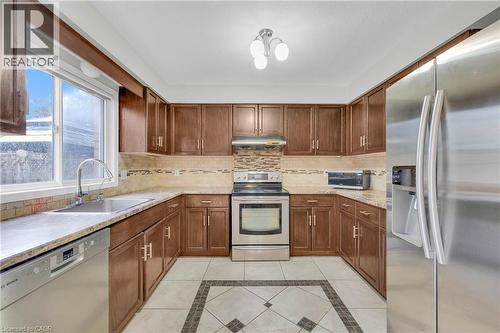 U-shaped kitchen featuring wood-finish cabinetry, light-toned countertops, and mosaic tile backsplash - 888 Paisley Road, Guelph, ON - Indoor Photo Showing Kitchen With Stainless Steel Kitchen