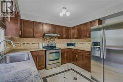 Kitchen featuring wood-finish cabinetry, stainless steel appliances, patterned tile flooring, and a stone-finish countertop - 