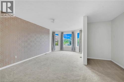 Spacious room featuring a prominent bay window, patterned accent wall, light-toned carpeting, white baseboards, and a neutral color palette - 888 Paisley Road, Guelph, ON - Indoor Photo Showing Other Room
