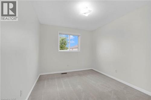 Neutral paint palette throughout, featuring a single window with white trim, light-colored carpeting, a ceiling-mounted light fixture, and white baseboards - 888 Paisley Road, Guelph, ON - Indoor Photo Showing Other Room