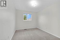 Neutral paint palette throughout, featuring a single window with white trim, light-colored carpeting, a ceiling-mounted light fixture, and white baseboards - 