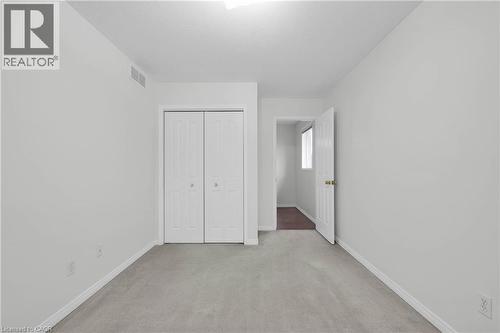 Carpeted room with light gray walls, featuring a bi-fold closet with white panels and gold-toned knobs - 888 Paisley Road, Guelph, ON - Indoor Photo Showing Other Room