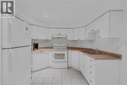 Kitchen featuring white cabinetry, white appliances, a double basin sink, light-toned countertops, and tiled flooring - 