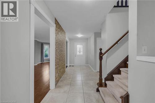 Foyer featuring light-toned tile flooring, a textured accent wall, and a wooden staircase with carpeted treads - 888 Paisley Road, Guelph, ON - Indoor Photo Showing Other Room
