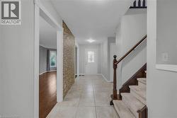 Foyer featuring light-toned tile flooring, a textured accent wall, and a wooden staircase with carpeted treads - 