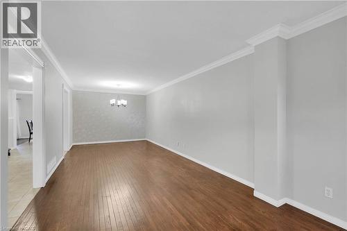 Spacious room featuring wood-finish flooring, light gray walls, white crown molding, and a modern chandelier - 888 Paisley Road, Guelph, ON - Indoor Photo Showing Other Room