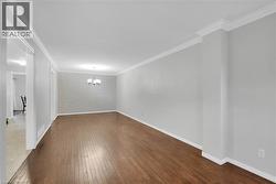 Spacious room featuring wood-finish flooring, light gray walls, white crown molding, and a modern chandelier - 