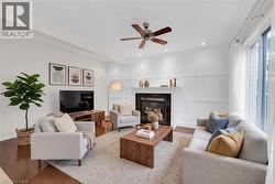 Living room featuring hardwood-finish flooring, a fireplace with a white mantel, recessed lighting, a ceiling fan, and large windows with white trim - 