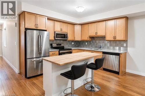 Kitchen featuring wood-finish flooring, stainless steel appliances, light wood cabinetry, gray tile backsplash, and a center island with a wood-finish countertop - 133 St Leger Street, Kitchener, ON - Indoor Photo Showing Kitchen With Stainless Steel Kitchen