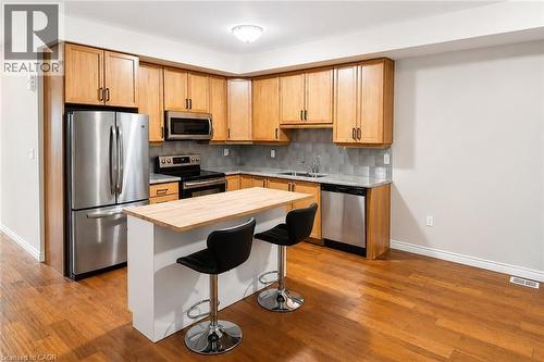 Kitchen featuring wood-finish cabinetry, stainless steel appliances, and a light-toned wood island with seating - 133 St Leger Street, Kitchener, ON - Indoor Photo Showing Kitchen With Stainless Steel Kitchen With Double Sink