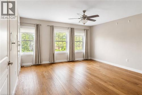 Spacious room featuring wood-finish flooring, three large windows, a ceiling fan with integrated lighting, and neutral wall tones - 133 St Leger Street, Kitchener, ON - Indoor Photo Showing Other Room