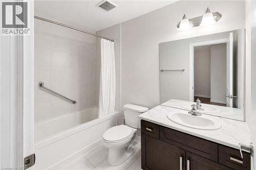 Full bathroom featuring a white porcelain tub with tiled surround, a toilet, and a vanity with a white countertop and dark wood-finish cabinetry - 133 St Leger Street, Kitchener, ON - Indoor Photo Showing Bathroom