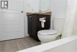 Bathroom featuring wood-finish tile flooring, a white paneled door, a dark wood-finish vanity with a light-colored countertop, and a white toilet - 