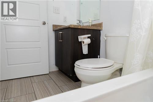 Bathroom featuring wood-finish tile flooring, a white paneled door, a dark wood-finish vanity with a light-colored countertop, and a white toilet - 190 Century Hill Drive Unit# A5, Kitchener, ON - Indoor Photo Showing Bathroom