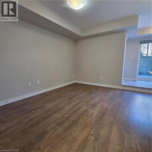 Expansive room featuring wood-finish flooring, light neutral wall paint, white baseboards, and a semi-flush mount ceiling light - 20 Palace Place Unit# E9, Kitchener, ON - Indoor Photo Showing Other Room