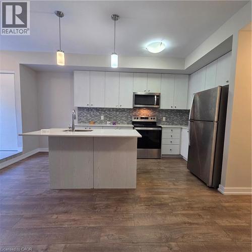 Modern kitchen featuring an island with an integrated sink, white cabinetry, a mosaic tile backsplash, and stainless steel appliances, all complemented by wood-finish flooring - 20 Palace Place Unit# E9, Kitchener, ON - Indoor Photo Showing Kitchen