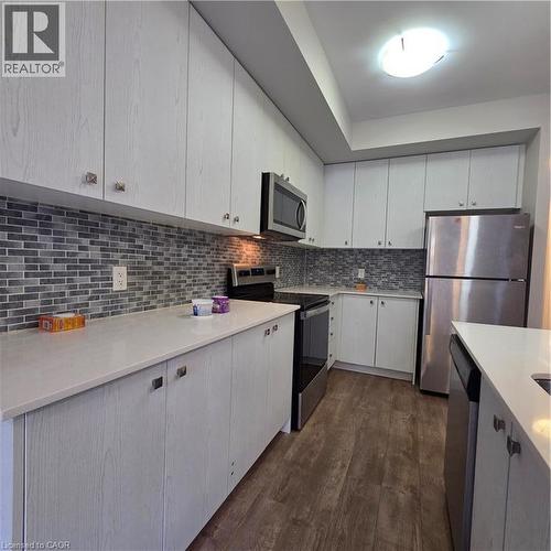 Modern kitchen featuring white wood-finish cabinetry, light-toned countertops, a mosaic tile backsplash, stainless steel appliances, and wood-finish flooring - 20 Palace Place Unit# E9, Kitchener, ON - Indoor Photo Showing Kitchen With Upgraded Kitchen