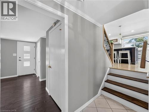 Entryway featuring dark wood-finish flooring, a modern white door with frosted glass panels, and a staircase with wood treads and a black metal spindle railing - 143 Cromwell Crescent, Hamilton, ON - Indoor Photo Showing Other Room