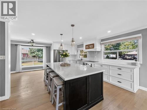 Kitchen featuring a large island with seating, white shaker cabinetry, stainless steel appliances, wood-finish flooring, and ample natural light from multiple windows - 143 Cromwell Crescent, Hamilton, ON - Indoor Photo Showing Kitchen With Upgraded Kitchen