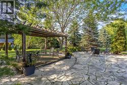 Expansive outdoor living area featuring a wood pergola over a deck, a large irregular flagstone patio, and mature evergreen trees - 