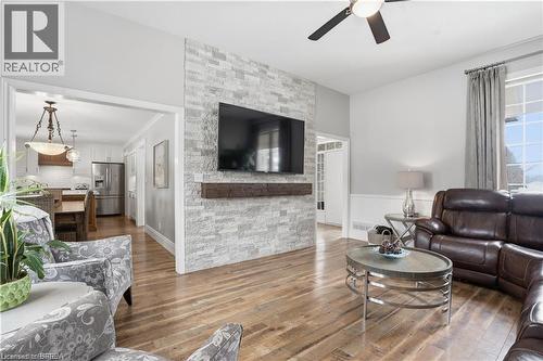 Living area featuring wood-finish flooring, a stacked stone accent wall with a wood mantel, a ceiling fan with integrated lighting, and an arched entryway - 25 Brian Drive, Burford, ON - Indoor Photo Showing Living Room