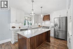 Contemporary kitchen featuring white shaker cabinetry, stainless steel appliances, a center island with a stone countertop, and wood-finish flooring - 