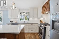 Kitchen featuring white cabinetry, subway tile backsplash, stainless steel appliances, a wood-finish range hood, and a kitchen island with a white countertop - 