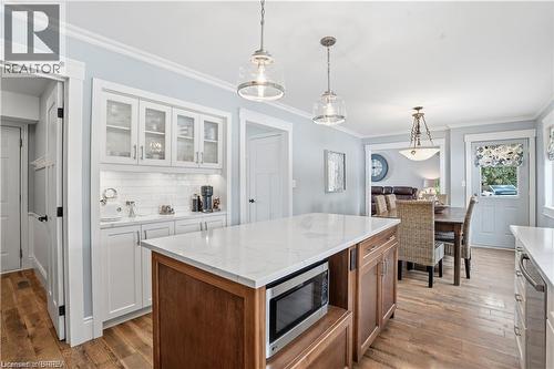 Open-concept kitchen featuring a central island with a built-in microwave, white shaker cabinetry with glass-front uppers, and wood-finish flooring - 25 Brian Drive, Burford, ON - Indoor Photo Showing Kitchen
