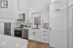 Contemporary kitchen featuring white cabinetry, stainless steel appliances, a paneled refrigerator, wood-finish flooring, and recessed lighting - 