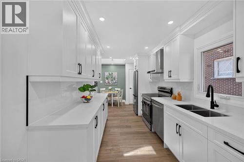 Sleek galley kitchen featuring extensive white cabinetry, white countertops, wood-finish flooring, a double basin sink with a matte black faucet, and stainless steel appliances - 101 Loyalist Drive, Hamilton, ON - Indoor Photo Showing Kitchen With Double Sink With Upgraded Kitchen