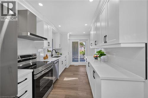 Galley kitchen featuring white cabinetry, stainless steel appliances, light countertops, wood-finish flooring, and recessed lighting - 101 Loyalist Drive, Hamilton, ON - Indoor Photo Showing Kitchen