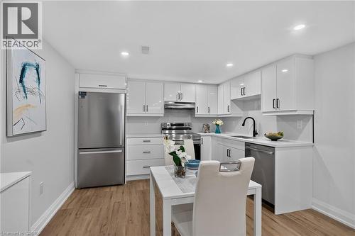 Modern kitchen featuring wood-finish flooring, white cabinetry with black hardware, stainless steel appliances, a black faucet, and recessed lighting - 101 Loyalist Drive, Hamilton, ON - Indoor Photo Showing Kitchen