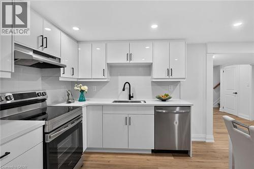 Contemporary kitchen featuring glossy white cabinetry, stainless steel appliances, a matte black faucet, recessed lighting, and wood-finish flooring - 101 Loyalist Drive, Hamilton, ON - Indoor Photo Showing Kitchen With Upgraded Kitchen