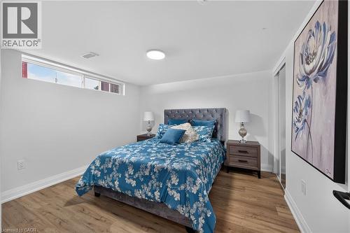 Bedroom featuring wood-finish flooring, a contemporary ceiling light fixture, a wide horizontal window, white baseboards, and a closet with sliding mirror doors - 101 Loyalist Drive, Hamilton, ON - Indoor Photo Showing Bedroom