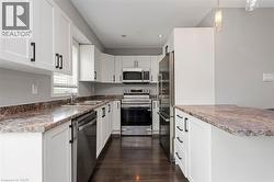 Kitchen featuring white shaker-style cabinetry with black hardware, wood-finish flooring, and stainless steel appliances - 