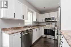 Kitchen with white shaker-style cabinetry, stainless steel appliances, and dark wood-finish flooring - 