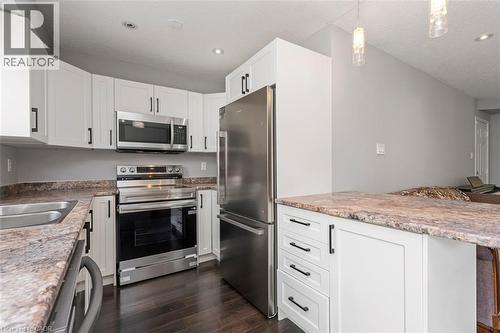 Modern kitchen featuring white cabinetry, dark wood-finish flooring, stainless steel appliances, a double basin sink, and a peninsula with countertop seating - 2248 Seton Crescent, Burlington, ON - Indoor Photo Showing Kitchen With Stainless Steel Kitchen With Double Sink With Upgraded Kitchen