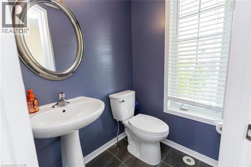 Powder room featuring a pedestal sink with a chrome faucet, oval wall mirror, toilet, and a window with blinds - 2248 Seton Crescent, Burlington, ON - Indoor Photo Showing Bathroom
