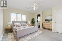 Neutral tone bedroom featuring a multi-pane window, flush-mounted ceiling fan, and light-colored carpeting - 
