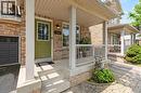 Brick exterior featuring a covered porch with white railing, a green paneled front door with glass insert, and an attached garage with a dark gray door - 2248 Seton Crescent, Burlington, ON  - Outdoor With Deck Patio Veranda 