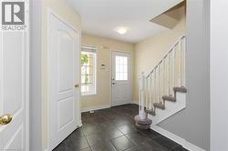 Entryway featuring dark square tile flooring, a white paneled door with a frosted glass insert, and a staircase with white balusters and carpeted treads - 