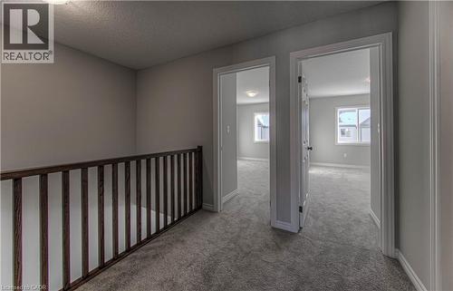 Carpeted hallway featuring a dark wood-finish railing, light grey walls, and two doorways opening into carpeted rooms with windows - 44 Harrison Drive, Cambridge, ON - Indoor Photo Showing Other Room