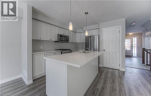 Modern kitchen featuring a central island with an undermount sink, pendant lighting, stainless steel appliances, light gray cabinetry, and wood-finish flooring - 44 Harrison Drive, Cambridge, ON - Indoor Photo Showing Kitchen With Double Sink With Upgraded Kitchen