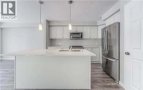 Contemporary kitchen featuring a spacious island with an undermount sink, pendant lighting, stainless steel appliances, white cabinetry, and wood-finish flooring - 44 Harrison Drive, Cambridge, ON - Indoor Photo Showing Kitchen With Stainless Steel Kitchen With Double Sink