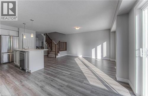 Open-concept living space featuring wood-finish flooring, a kitchen island with pendant lighting, stainless steel appliances, and a staircase with wood railings - 44 Harrison Drive, Cambridge, ON - Indoor Photo Showing Kitchen